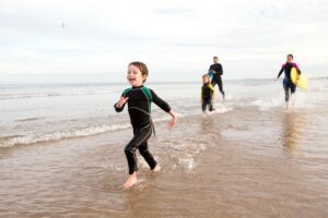 A young boy joyfully splashes through the water while his family enjoys a surfing session.