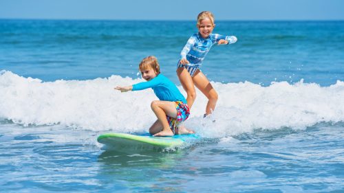 Two young surfers ride with fun on one surfboard
